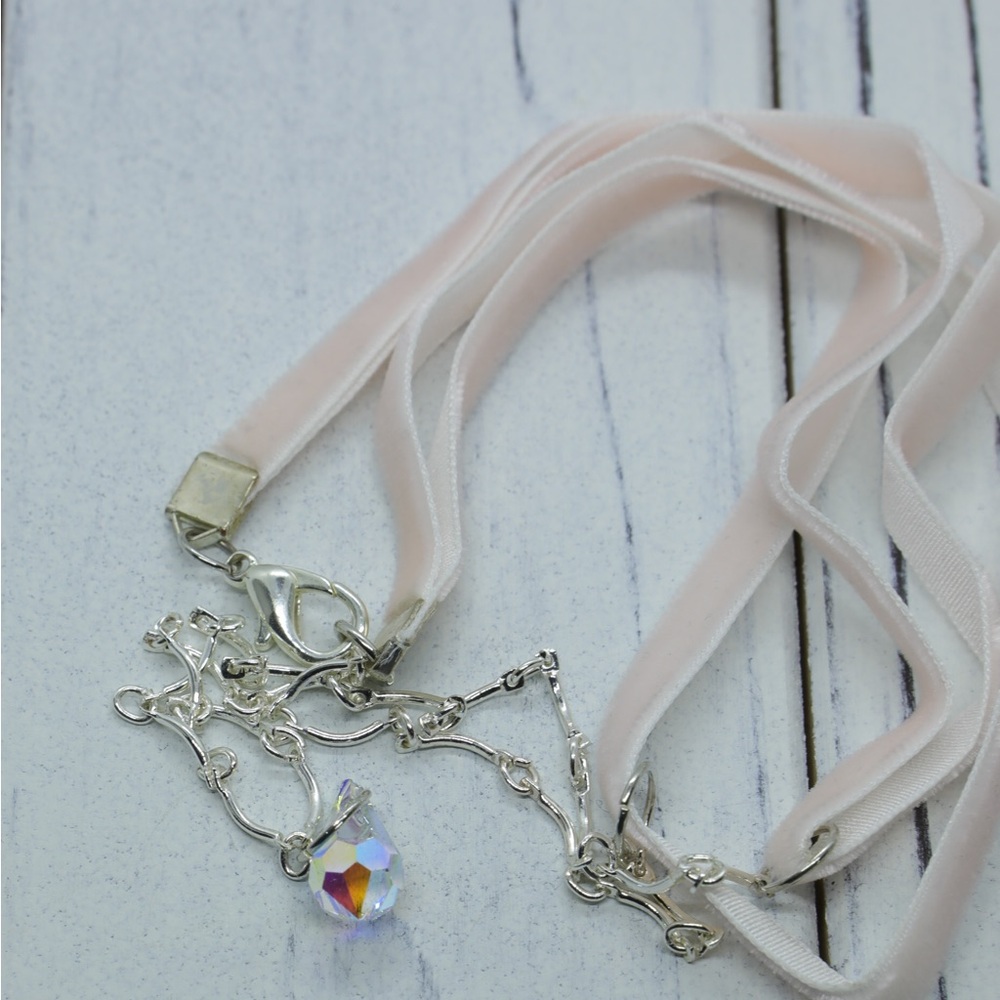 A small crystal tear pendant on a pink velvet and silver tone chain.